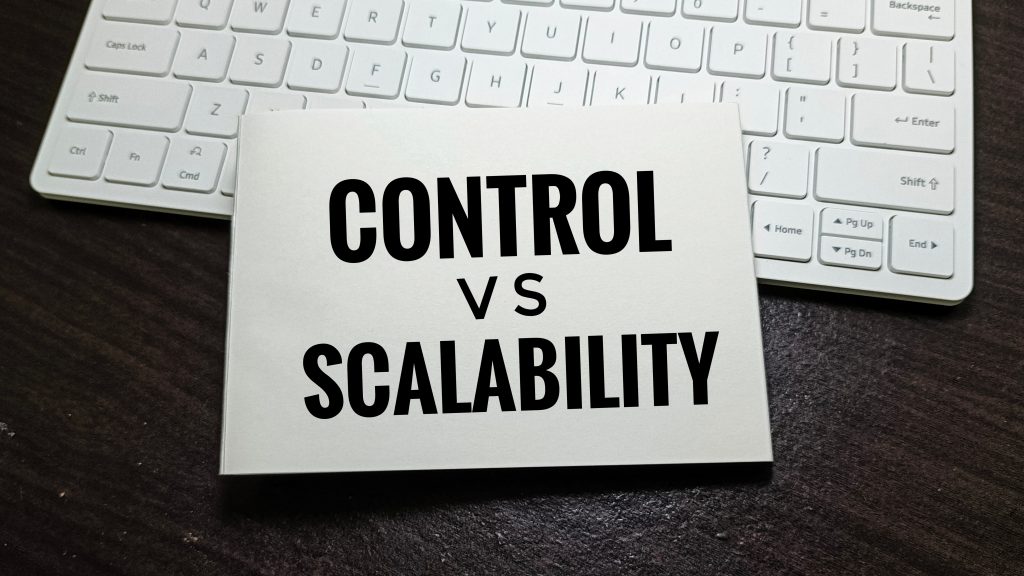 A white card on a dark wooden desk, in front of a white keyboard, reads “CONTROL VS SCALABILITY” in bold black text.